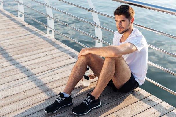 Sportsman with bottle of water sitting and relaxing on pier - Foto, Bild