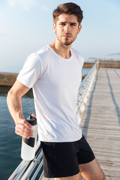 Sportsman standing on pier and holding bottle of water - Foto, imagen