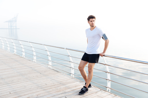 Man athlete with armband and cell phone standing on pier - Foto, Imagem