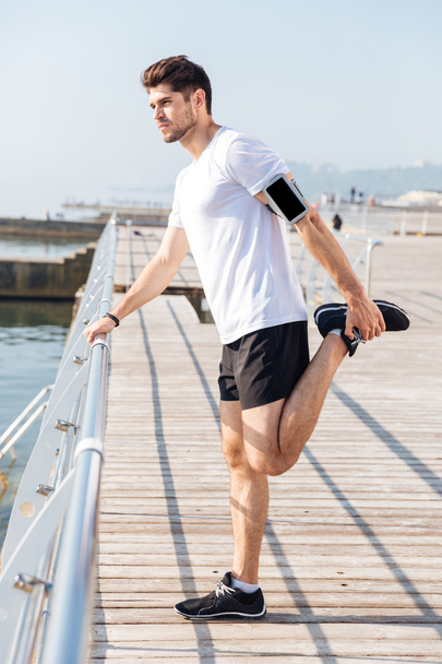 Young sportsman stretching legs during workout on pier - Foto, Bild