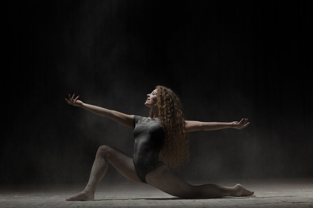 Flexible woman dancing with flour on black background - Foto, afbeelding