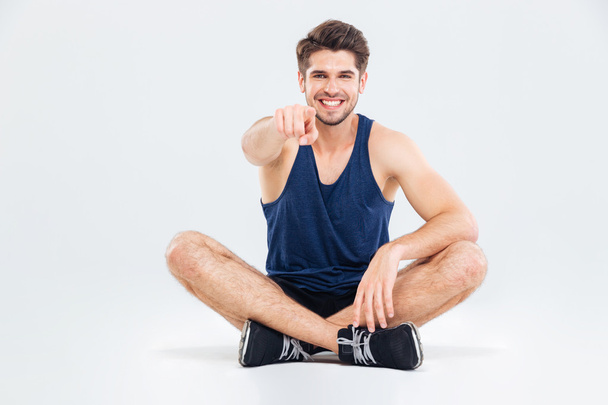 Cheerful sportsman sitting with legs crossed and pointing on you - Fotografie, Obrázek