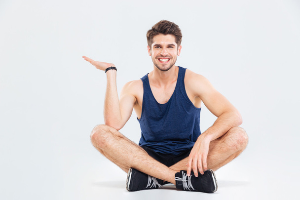 Happy young athletic man sitting and holding copyspace on palm - Zdjęcie, obraz