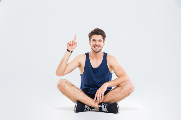 Cheerful man athlete sitting with legs crossed and pointing up - Photo, image
