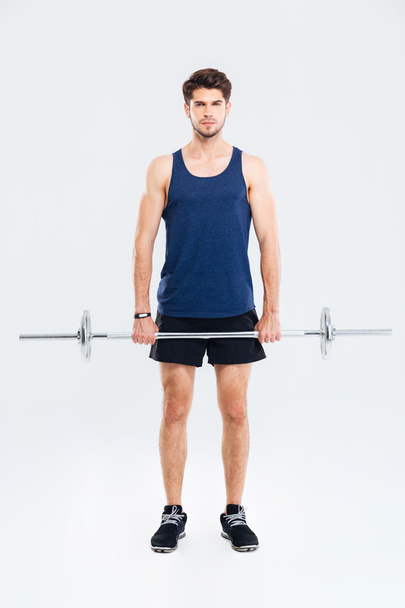 Full length of serious young sportsman exercising with barbell - Foto, Bild