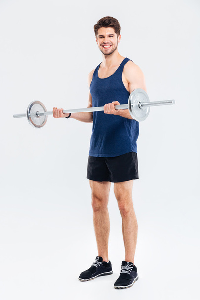 Happy young man athlete standing and training with barbell - 写真・画像