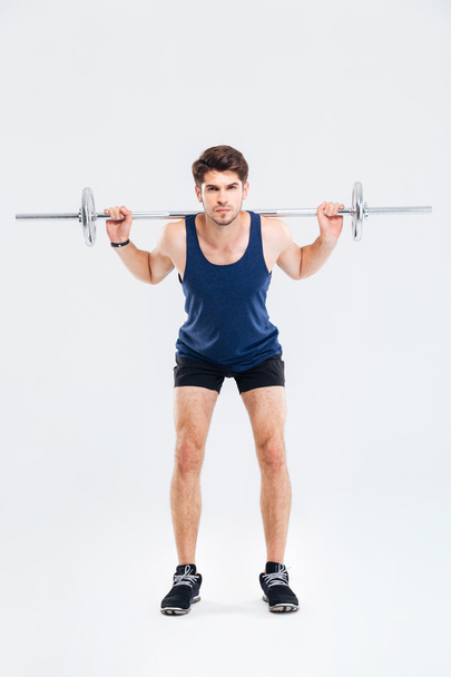 Serious young man athlete standing and exercising with barbell - Foto, Bild