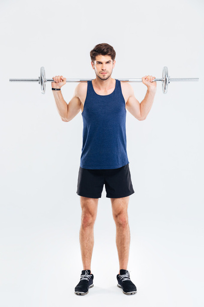 Concentrated young sportsman standing and working out with barbell - 写真・画像