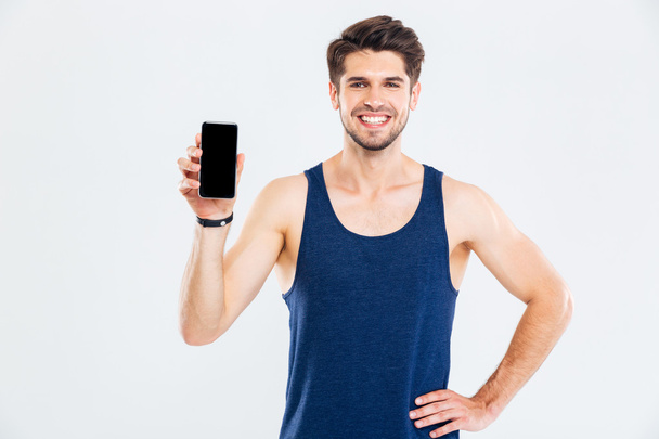 Cheerful young sportsman standing and holding blank screen mobile phone - 写真・画像