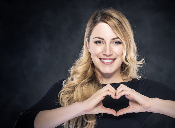 Portrait of beautiful young blond woman showing heart sign. - Fotoğraf, Görsel