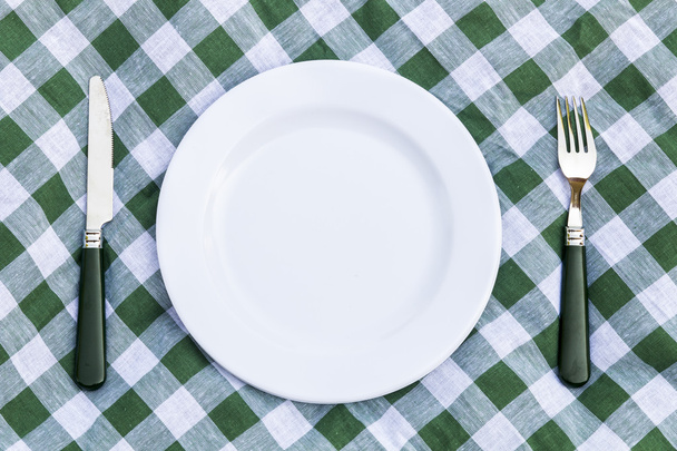 ナイフ、白い皿と緑ピクニック テーブル クロスの上のフォーク。フラットを置く - 写真・画像