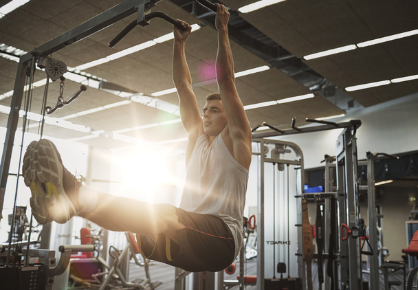 man flexing abdominal muscles on pull-up bar - Фото, зображення