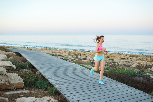 Giovane donna atletica che corre lungo un sentiero in riva al mare
 - Foto, immagini