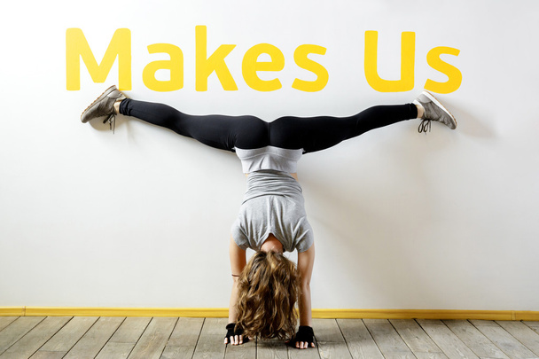 Fit woman doing a handstand near the wall below the phrase "Makes Us".  - Fotografie, Obrázek