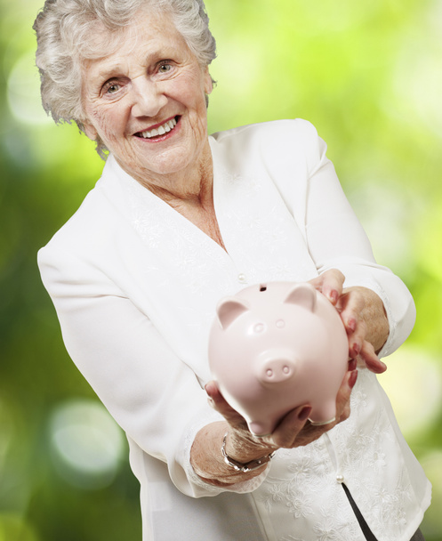 Portret van senior vrouw toont een piggy bank tegen een natuur-b - Foto, afbeelding