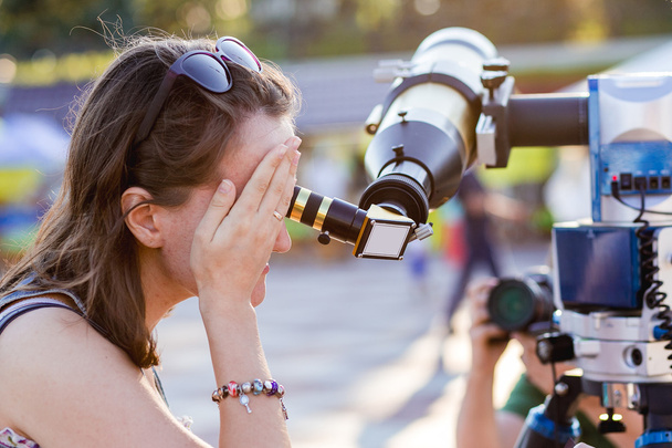 Νεαρή γυναίκα κοιτάζει μέσα από τηλεσκόπιο ηλιακή - Φωτογραφία, εικόνα