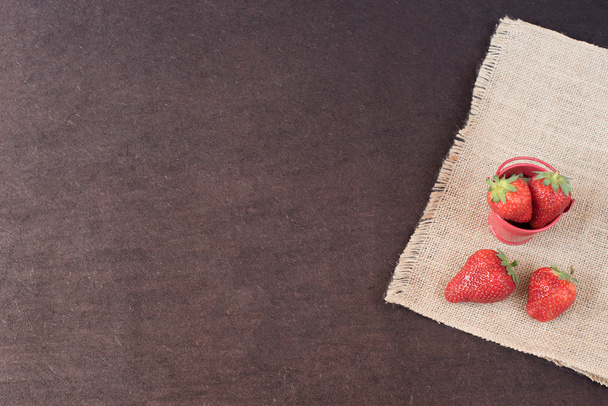Fresh strawberries in mini metal bucket on hessian jute. Black background.  - Foto, imagen
