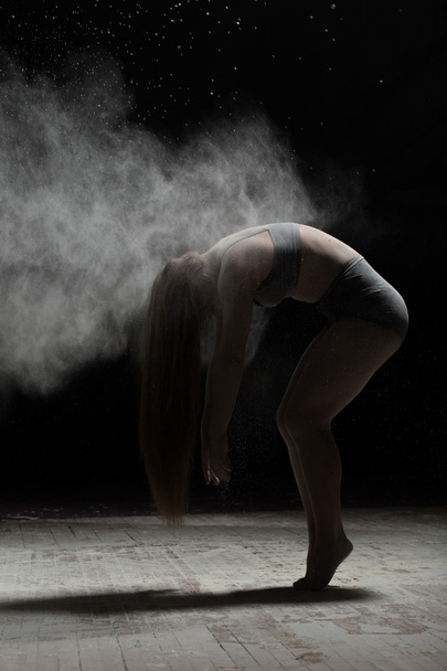 Flexible woman posing with flour on black background - Фото, изображение
