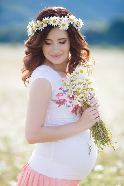 eine schwangere Frau auf einem Feld mit einem Strauß weißer Gänseblümchen - Foto, Bild