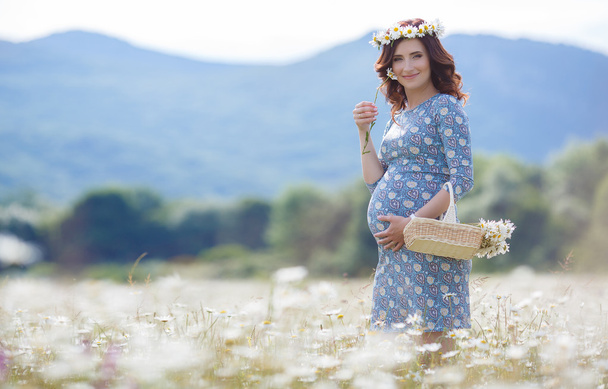 Pregnant woman in field with basket of white daisies - Fotó, kép