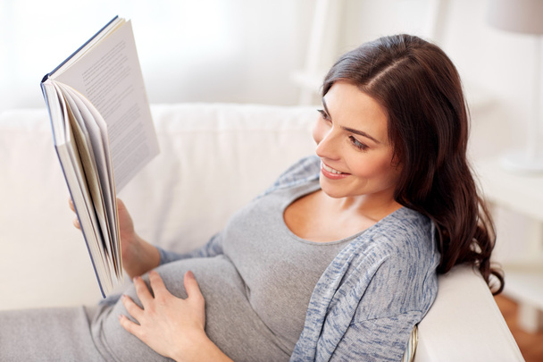 happy pregnant woman reading book at home - 写真・画像