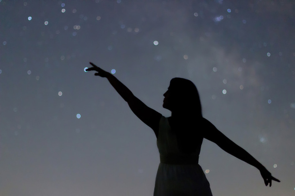 Silhouette einer tanzenden Frau, die in den Nachthimmel zeigt. Frauensilhouette unter sternenklarer Nacht, verschwommene Milchstraßengalaxie.  - Foto, Bild