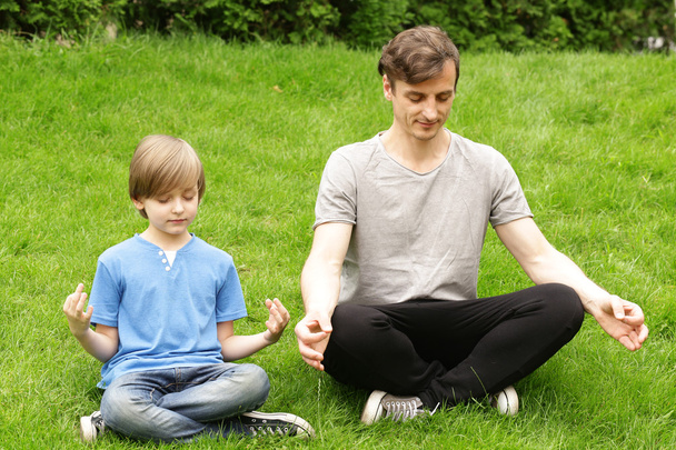 father and son sitting on green grass and meditates - Photo, Image