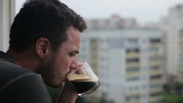 Young man drinking coffee and using smartphone on balcony - Filmmaterial, Video