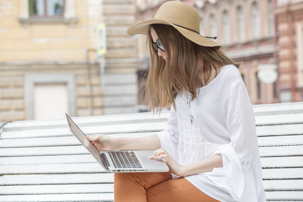 Happy young woman working with a laptop sitting on a bench.  - Foto, Imagen
