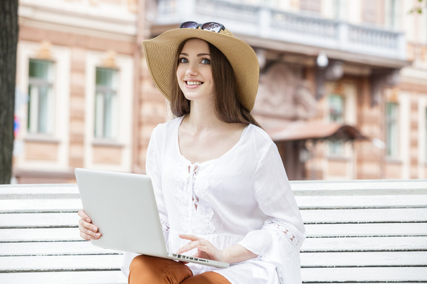 Happy young woman working with a laptop sitting on a bench.  - Фото, зображення