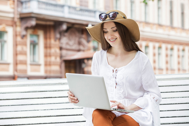 Happy young woman working with a laptop sitting on a bench.  - Foto, Bild