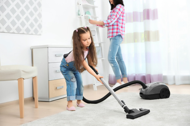 Daughter and mother using vacuum cleaner in room - Foto, Bild