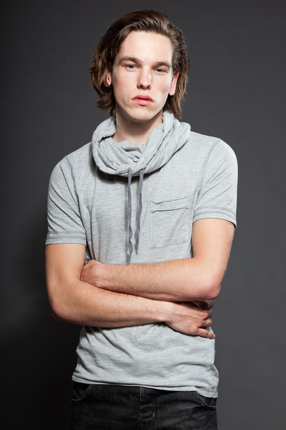 schöner junger Mann mit braunen langen Haaren, graues Hemd auf grauem Hintergrund. Modestudio gedreht. Gesichtsausdruck. - Foto, Bild