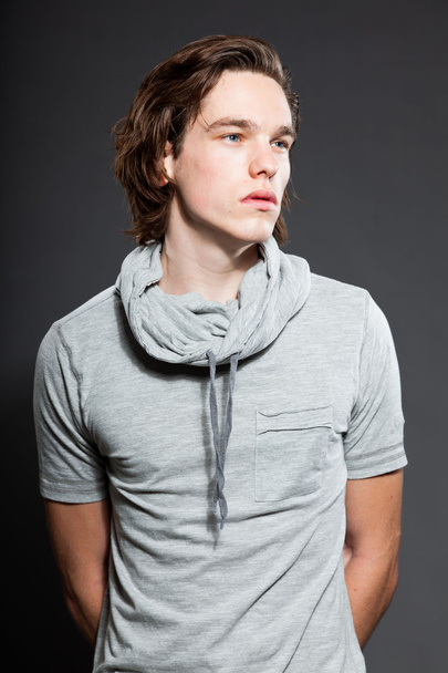 Handsome young man with brown long hair wearing grey shirt isolated on grey background. Fashion studio shot. Expressive face. - Foto, immagini
