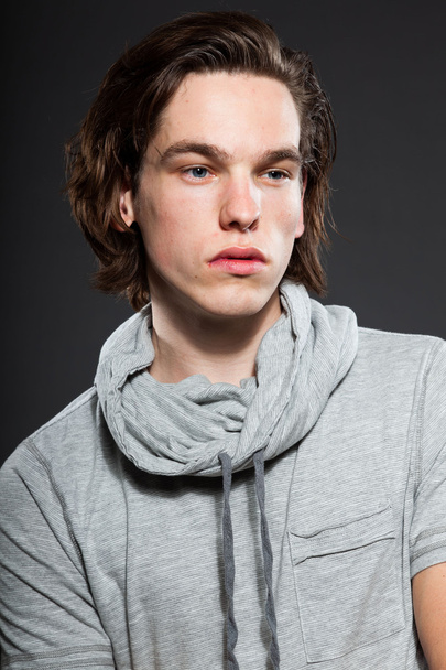 Handsome young man with brown long hair wearing grey shirt isolated on grey background. Fashion studio shot. Expressive face. - Φωτογραφία, εικόνα