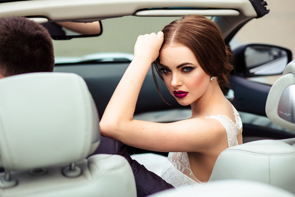 gorgeous bride with fashion makeup and hairstyle in a luxury wedding dress in a white cabriolet car - Φωτογραφία, εικόνα
