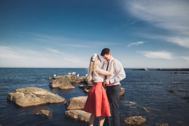 Romantic loving couple posing on stones near sea, blue sky - Фото, зображення