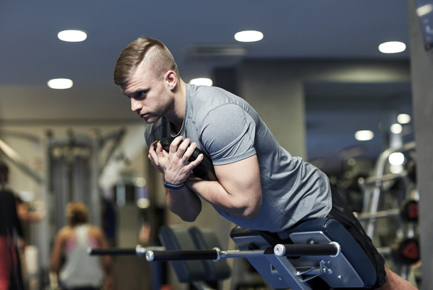 młody człowiek zginając plecy mięśnie na ławce w siłowni - Zdjęcie, obraz