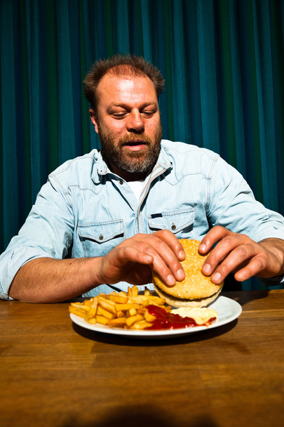 Man with beard eating fast food meal. Enjoying french fries and a hamburger. - Foto, afbeelding