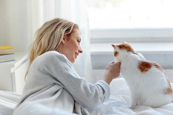 happy young woman with cat in bed at home - Photo, image
