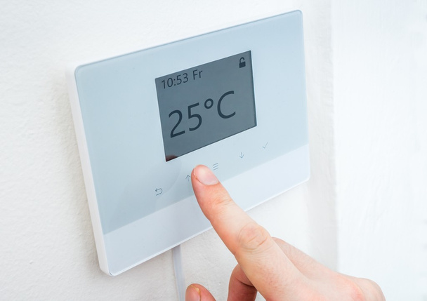 Concepto de calefacción. La mano está ajustando la temperatura en la habitación en el control digital del termostato central
. - Foto, imagen