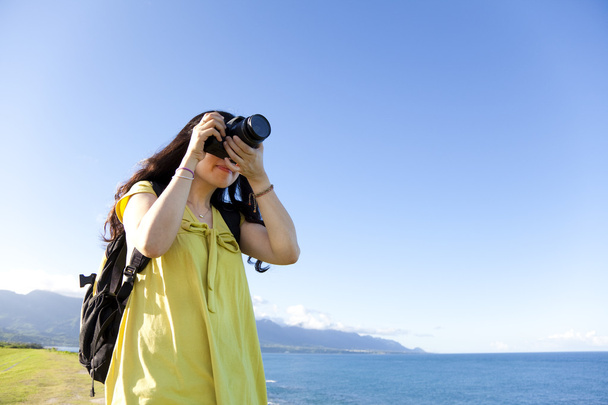 Nuori nainen reppu seisoo kukkulalla ottamassa valokuvaa
 - Valokuva, kuva