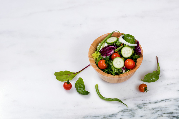 frischer Salat in Holzschale auf weißem Marmorstein - Foto, Bild