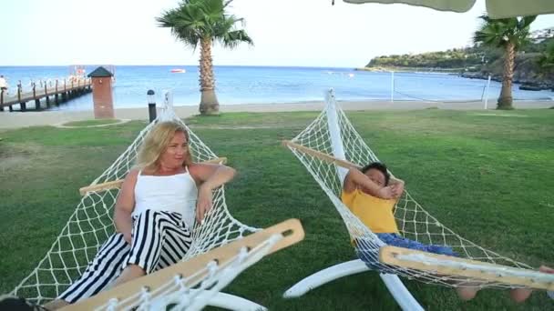 Mother and son relaxing in a hammock near the sea - Felvétel, videó