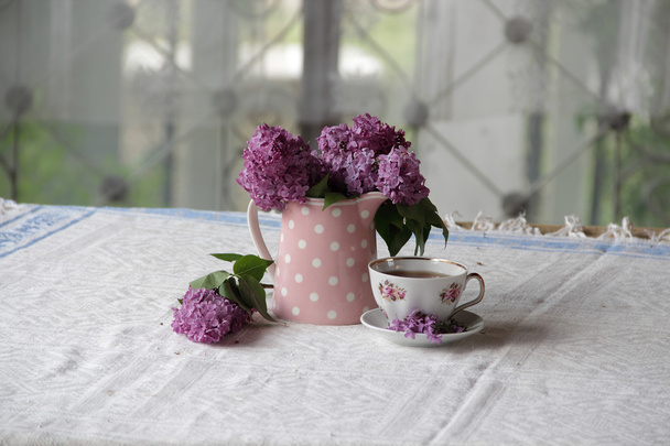 a Cup of tea and a bouquet of lilacs on the table - Valokuva, kuva