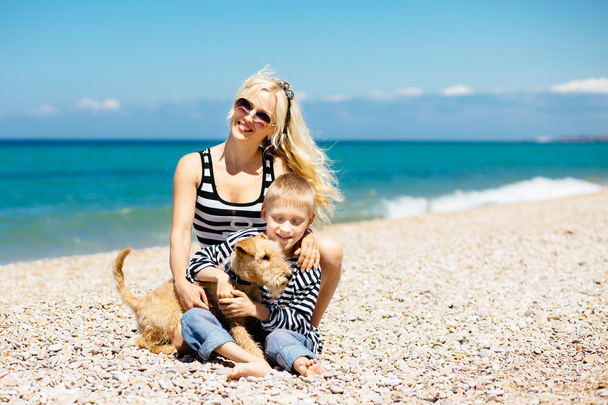 Beautiful young woman and her son playing with puppy on the beach - Fotoğraf, Görsel