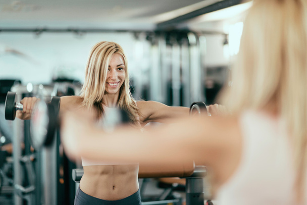 vrouw oefenen met gewichten voor spiegel - Foto, afbeelding