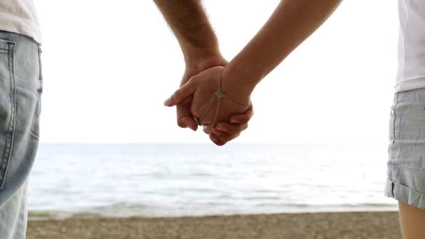Couple holding hands on the background of the sea. Close-up of hands against the sea. Man and woman holding hands on the beach. Love, romance, newlyweds.  - Footage, Video