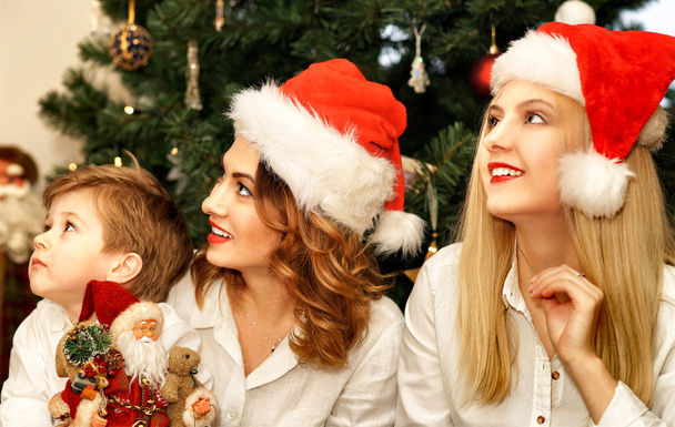 Prachtige familie in rode Santa hoeden bij de kerstboom - Foto, afbeelding