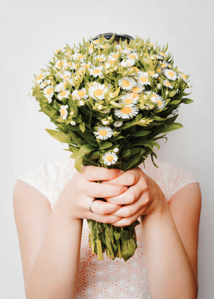 Girl with bouquet of camomile at white wall - Fotó, kép
